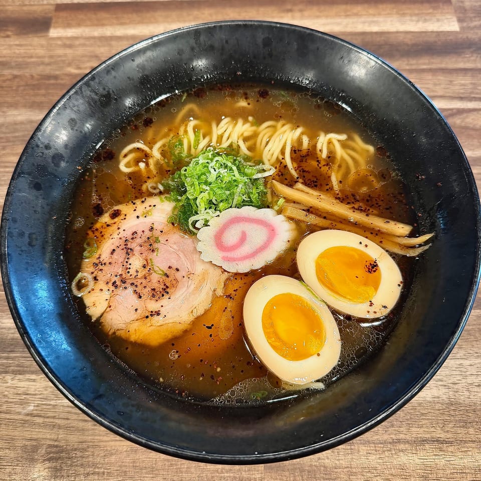 Japanese ramen bowl with noodles, sliced pork, soft-boiled eggs, bamboo shoots, green onions, and fish cake in broth.