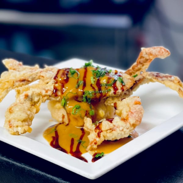 Crispy fried soft-shell crab drizzled with orange and dark sauces, garnished with green onions.