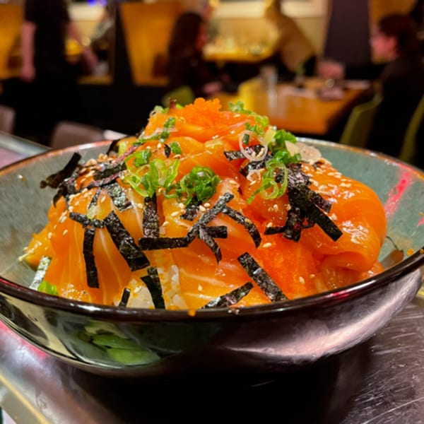 A vibrant salmon sushi bowl with roe, nori, and scallions, served in a dark bowl.