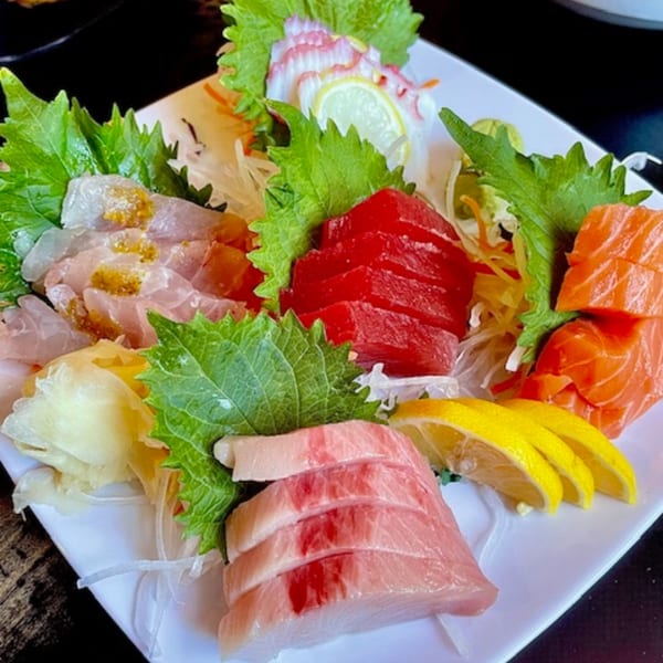 A colorful sashimi platter with various fish, octopus, lemon, and green garnishes on a white plate.