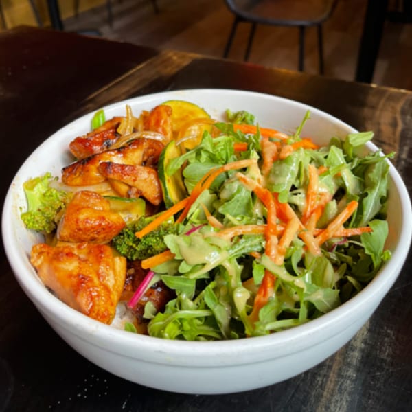 Teriyaki chicken, broccoli, zucchini, and a fresh green salad with carrots in a white bowl.